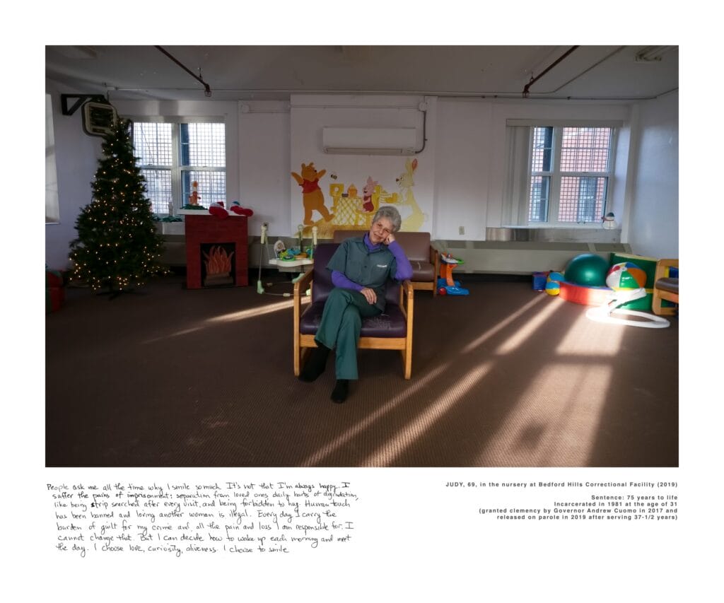 A photo of an older woman sat on a chair inside a detention facility.