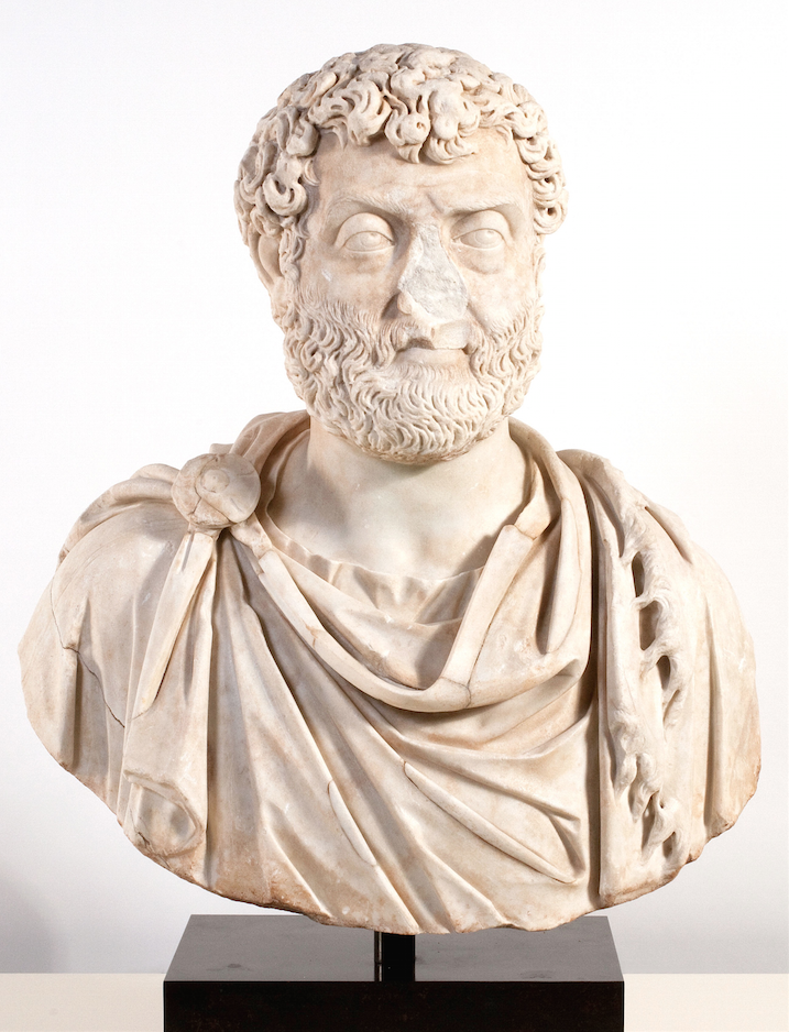 Roman marble bust of gentleman with curly hair, wearing Roman attire. The nose is broken off.