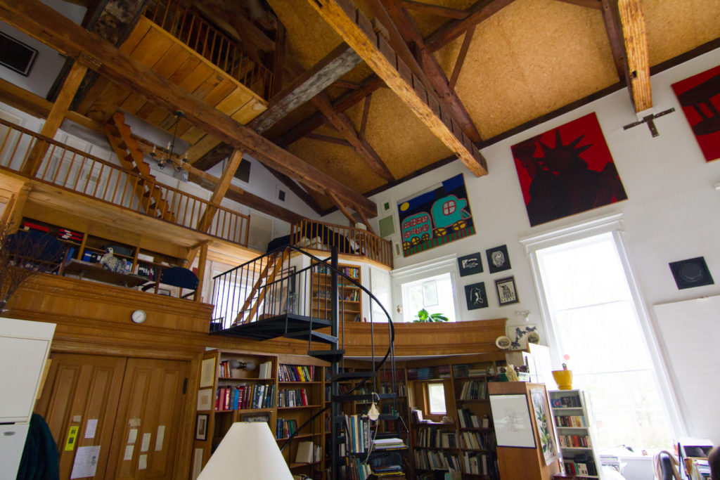 Eleanore Mikus’ home/studio. A room made of wood and a tall white wall on the right with books/paintings everywhere