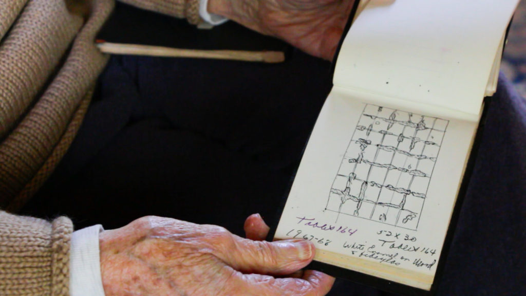 A hand holding a notebook with a grid-like sketch drawn on it