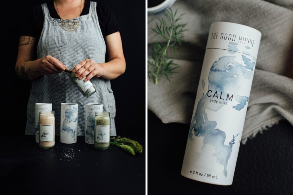 Left: Person scooping bath/body/home product out of a glass jar. On the table are other jars of glass and printed metal. Right: A close up of one of the printed metal jars lying on a black table with a gray cloth and a sprig of herb. Printed on the container is "THE GOOD HIPPIE", "CALM", "body mist", "e 2 fl oz / 59 mL" on a white background with blue watercolor splash.
