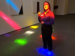 Photograph of a Blanton gallery assistant posing in the colorful lights projected from Ellsworth Kelly's "Austin"