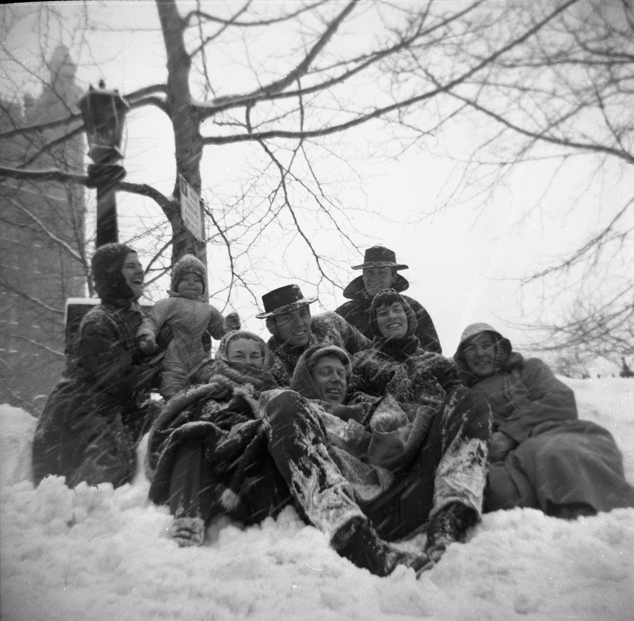 Photo of a group of New York artists, including Ellsworth Kelly, Robert Indiana and Agnes Martin, posed together sitting in the snow.