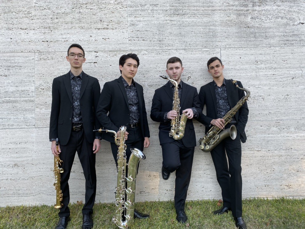 Four saxophone players in matching suits and shirts. Saxophone types left to right: soprano, bass, alto, and tenor.