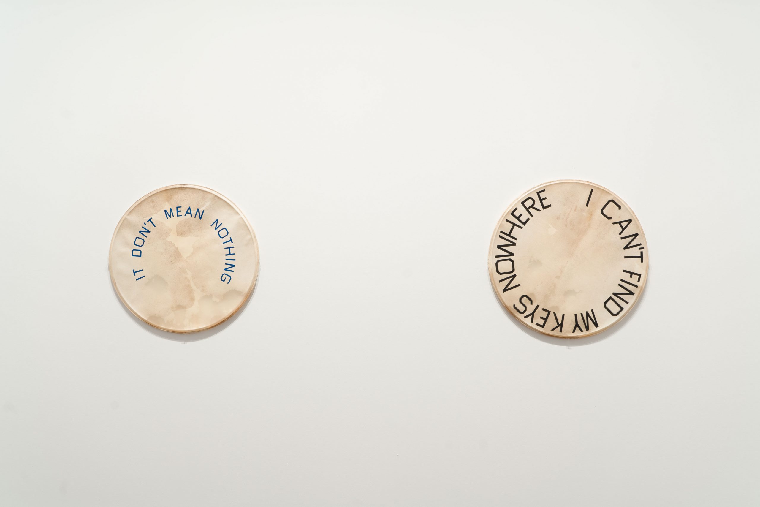 Photo of two drum skins hanging on the wall with writing on, taken during the installation of Ed Ruscha: Drum Skins exhibition at the Blanton Museum of Art.