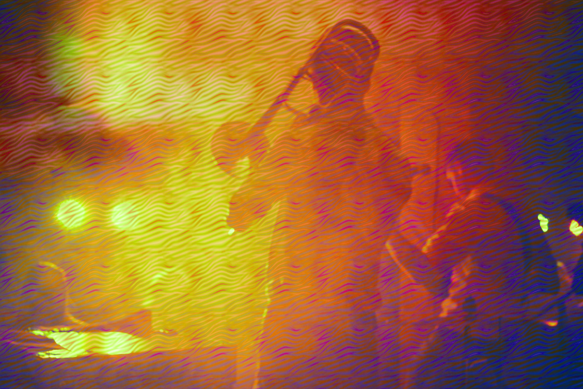Image of back of band the visible instrument is a the back of a trombone the image is all orange and yellow distorting the image of the band members to give a hazy quality
