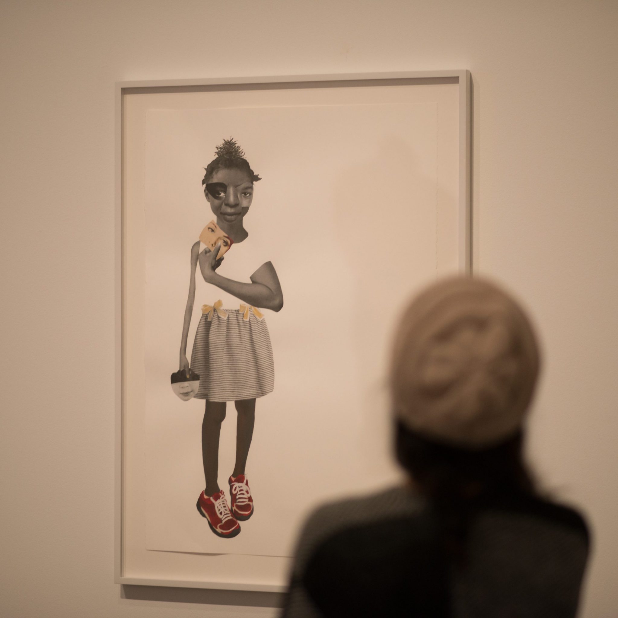 A person wearing a hat looking at a collage of a young Black girl on the wall
