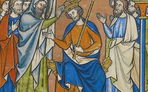 a man pours a substance on the head of a seated man wearing a crown and holding a staff while several other men watch