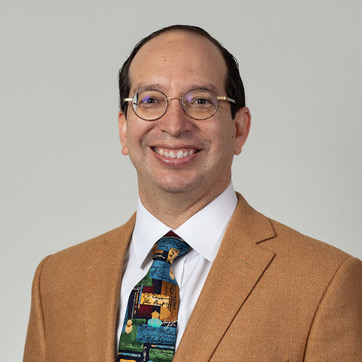 A man wearing glasses with a tan suit jacket.