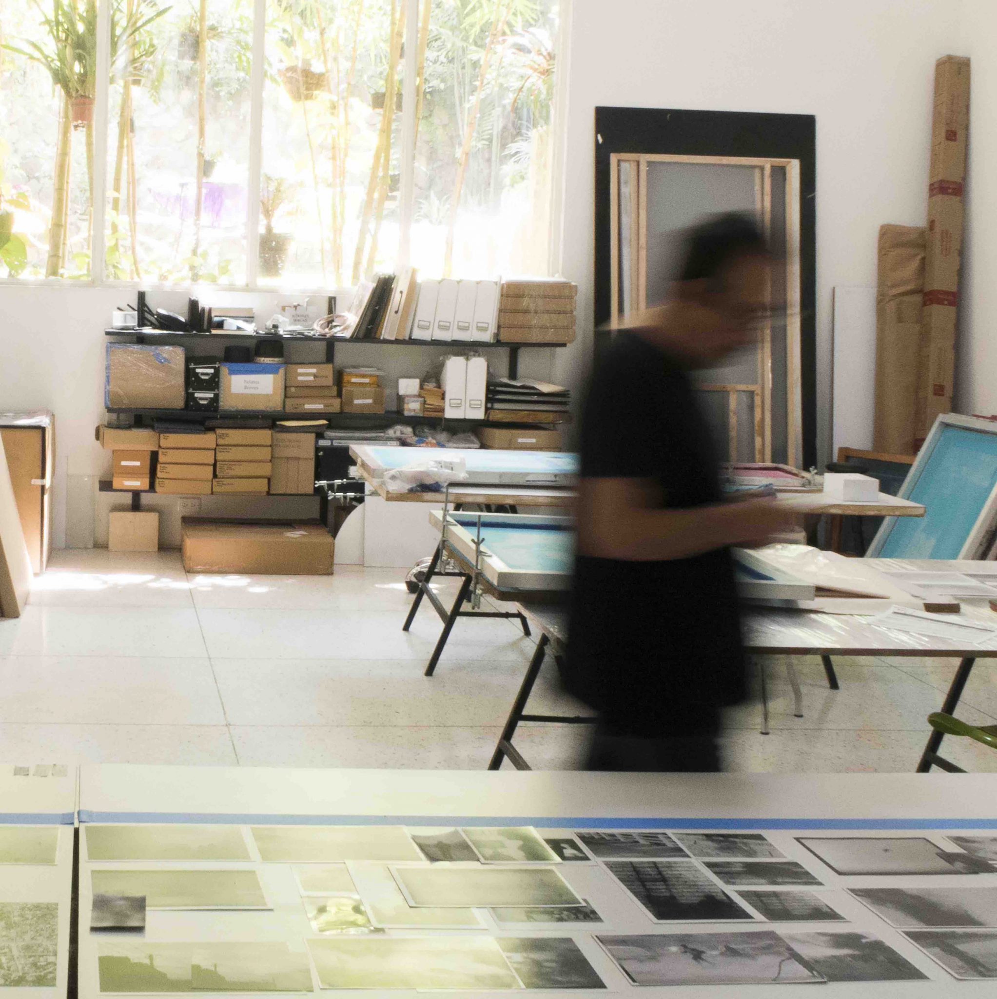 A blurred image of a man walking past a table of photos inside a studio.