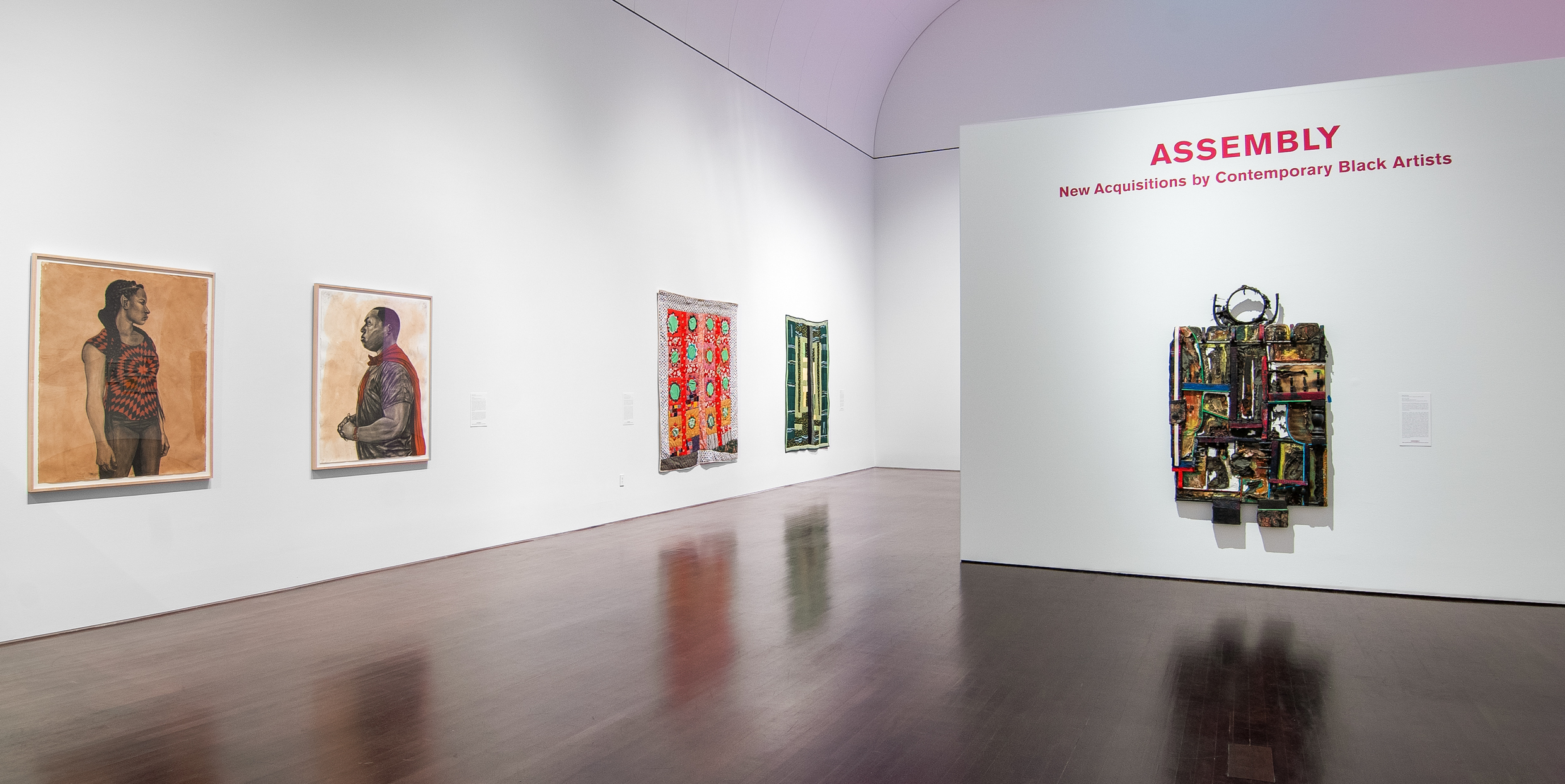 A wide shot of several different artworks hung on gallery walls. The title of the show is written above one work 