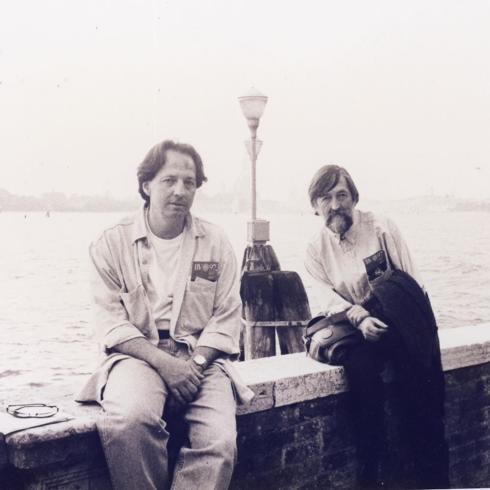 Fotografía en blanco y negro de dos personas sentadas. Detrás de ellos, hay dos faroles y, al fondo, el mar.