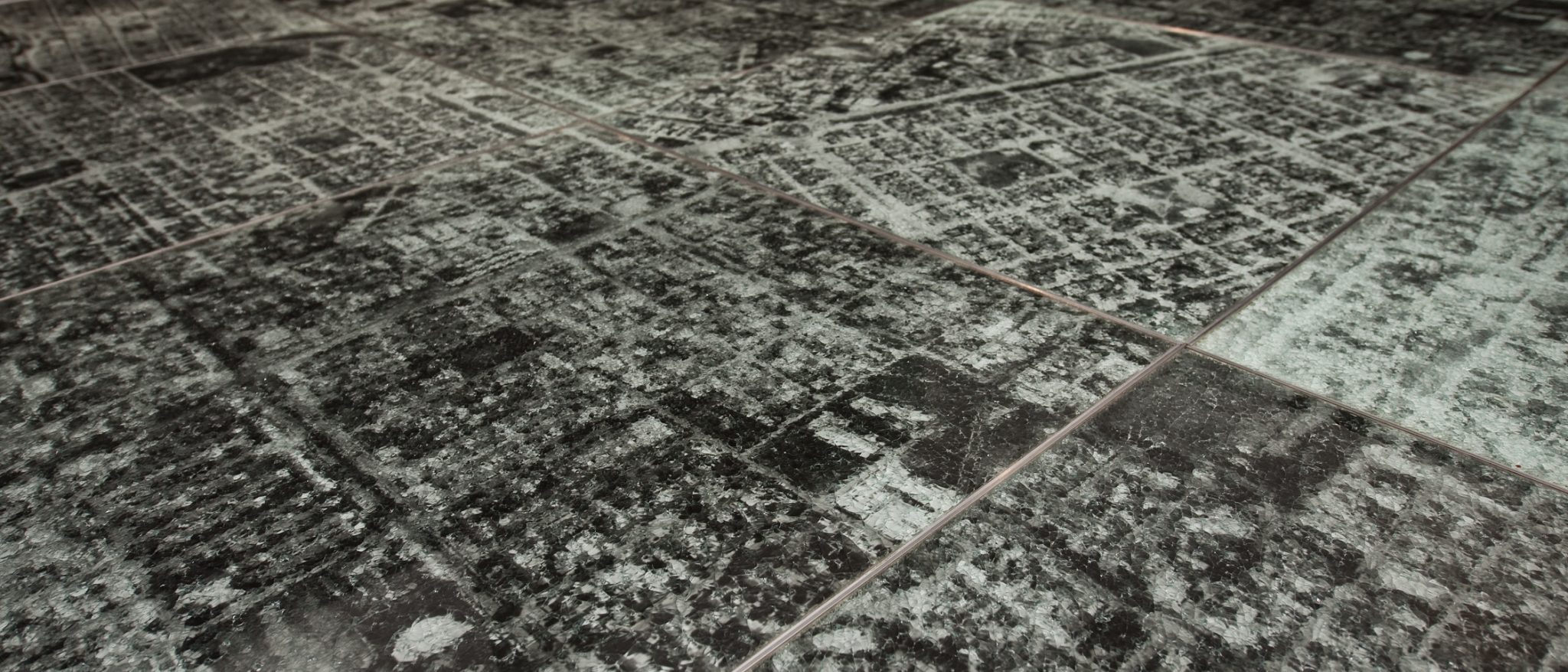 Fotografía aérea en blanco y negro de una ciudad, dividida en segmentos cuadrados colocados juntos en una cuadrilla sin orden pre-establecido.