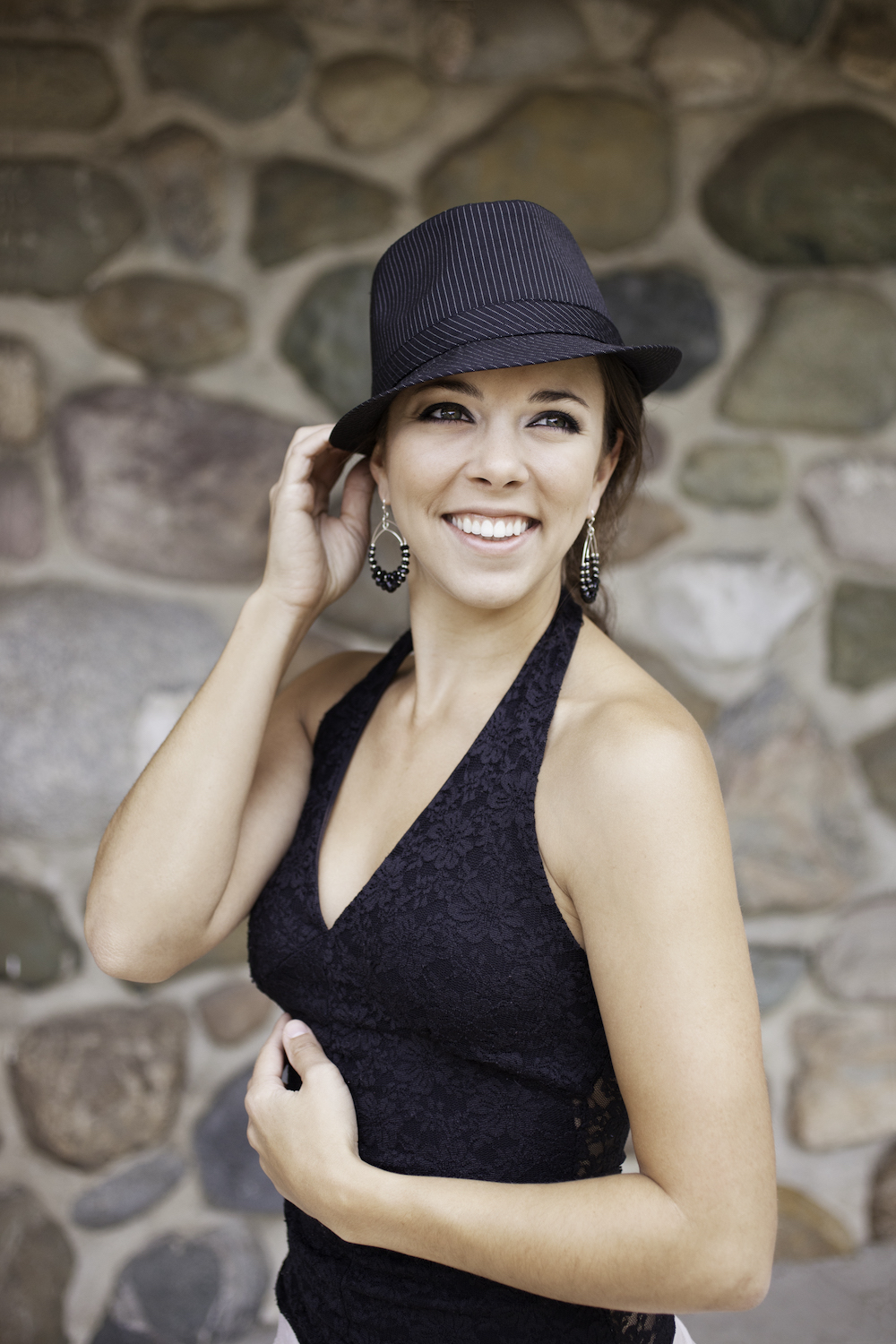 A woman wearing a black halter-neck top and a black hat, smiling