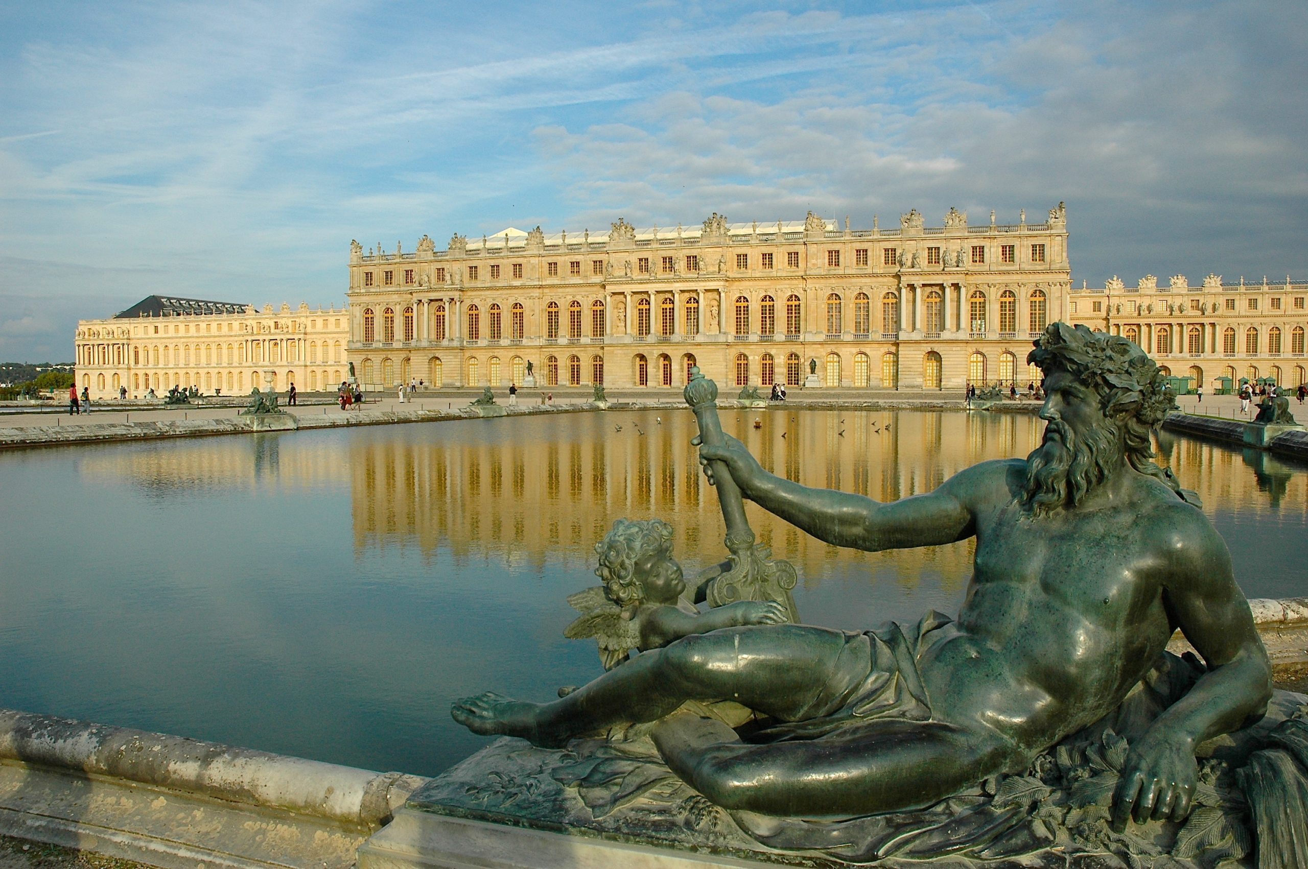 A view of the palace of Versaille in France. In the foreground is a statue of a God layout down