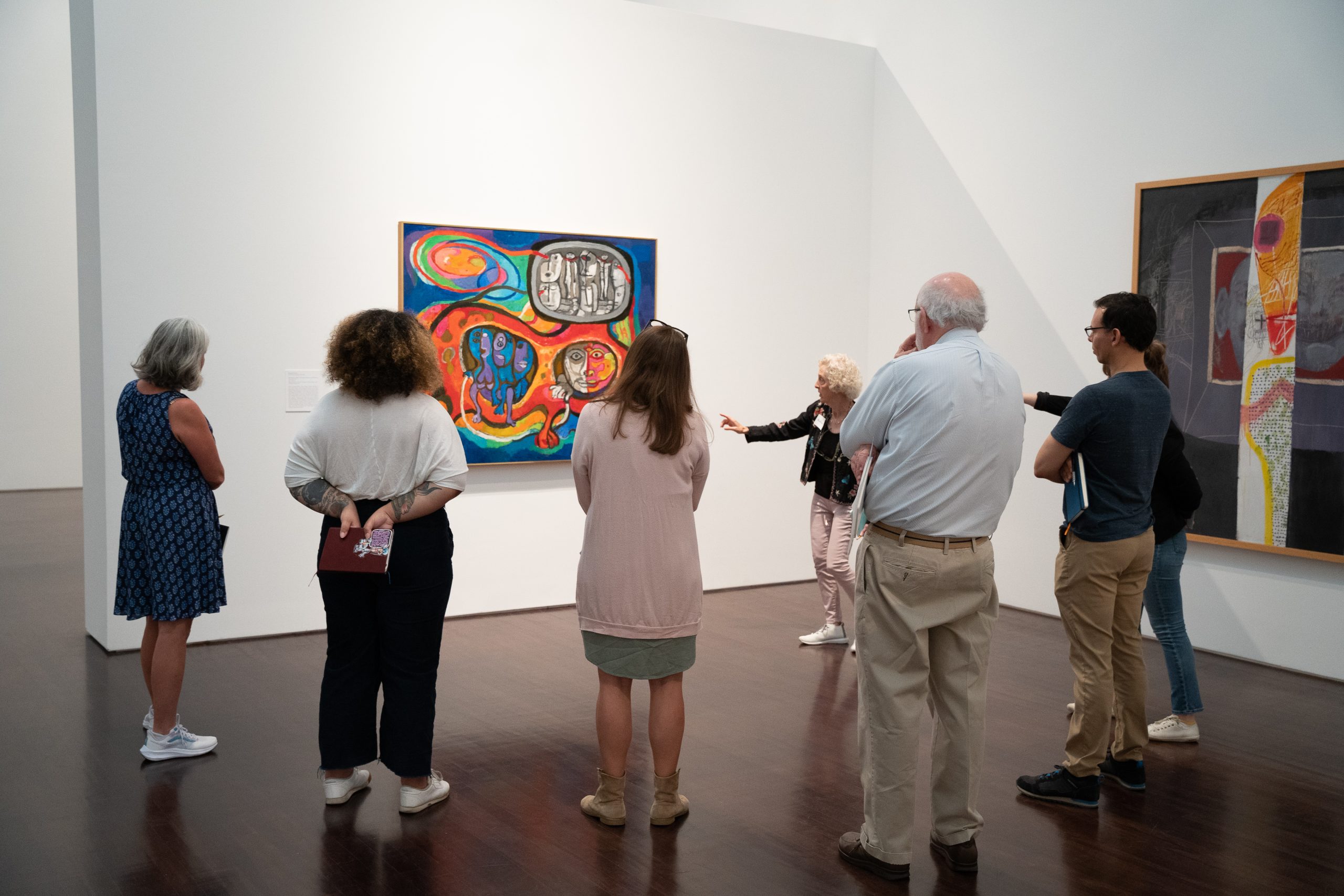 A group of people looking at abstract artwork in a gallery. A teacher gestures to the painting