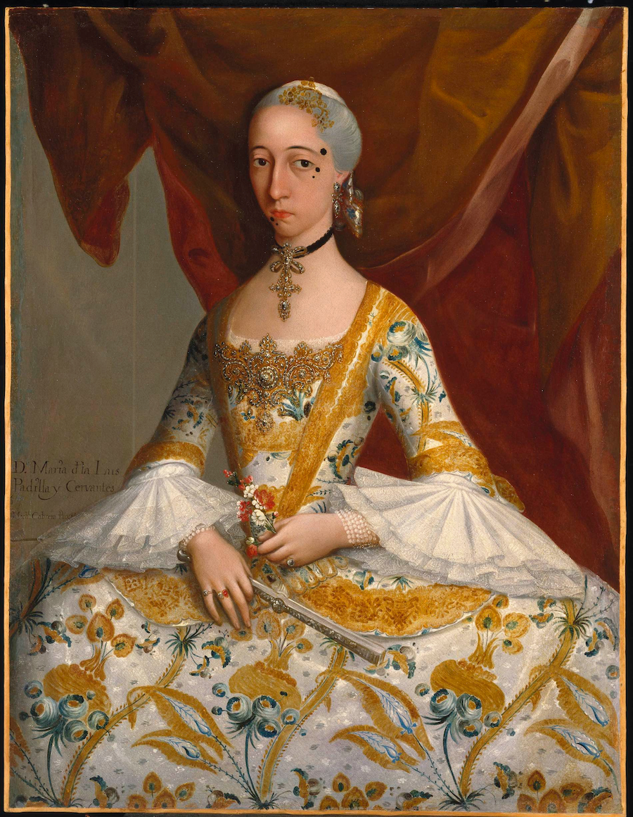A woman wearing an ornate 18th-century dress with laced sleeves, clutching a fan.