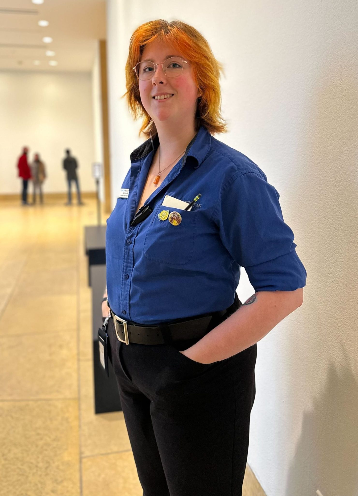A person in a gallery wearing a blue shirt and name badge and an earpiece