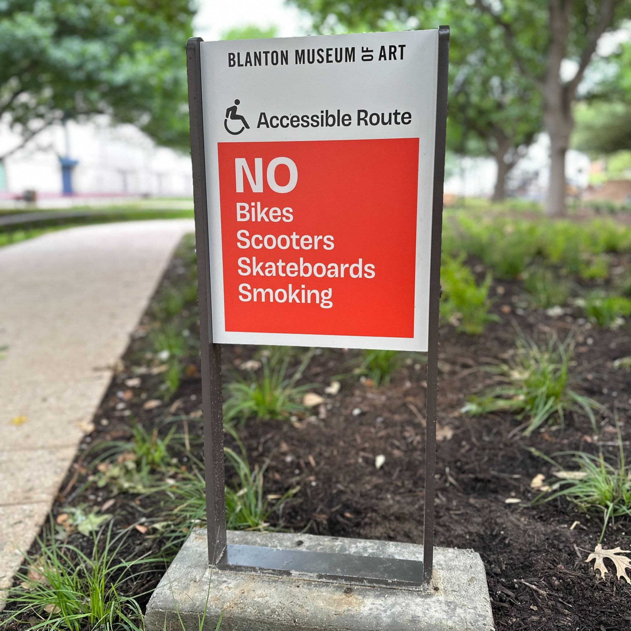 A sign on museum grounds reading "Blanton Museum of Art, Accessible Route. NO Bikes, scooters, skateboards, smoking