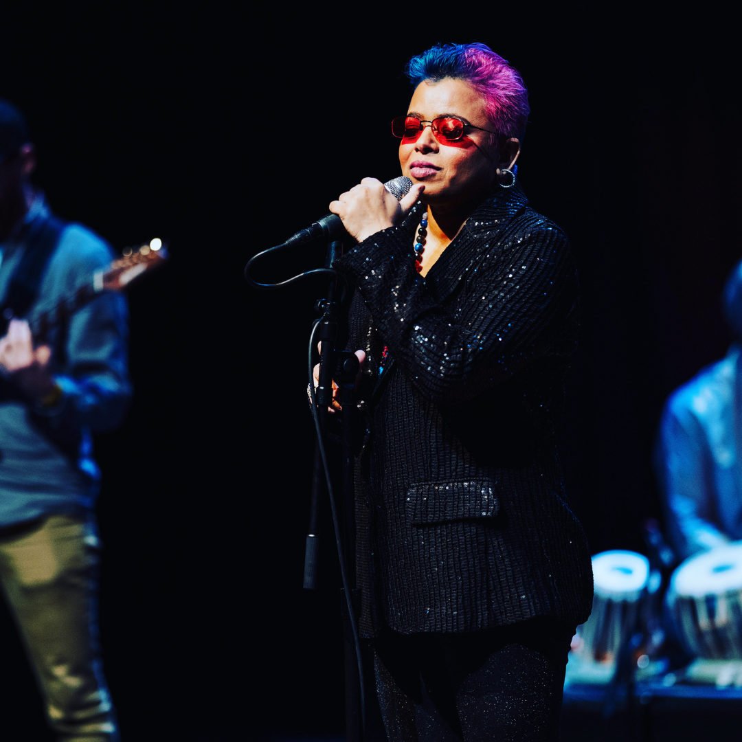A person with short pink hair singing into a microphone