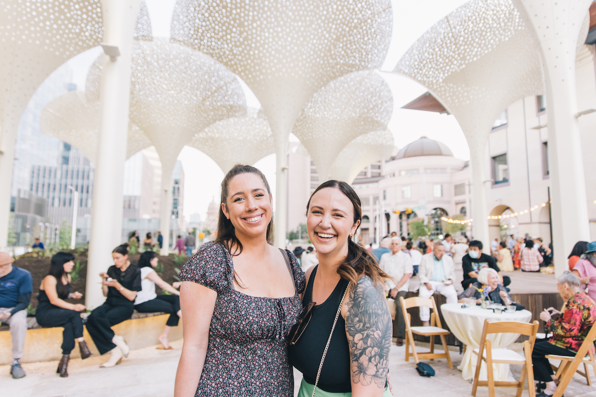 Two people smiling with tall petal-like structures in the background on the Blanton Museum of Art's grounds