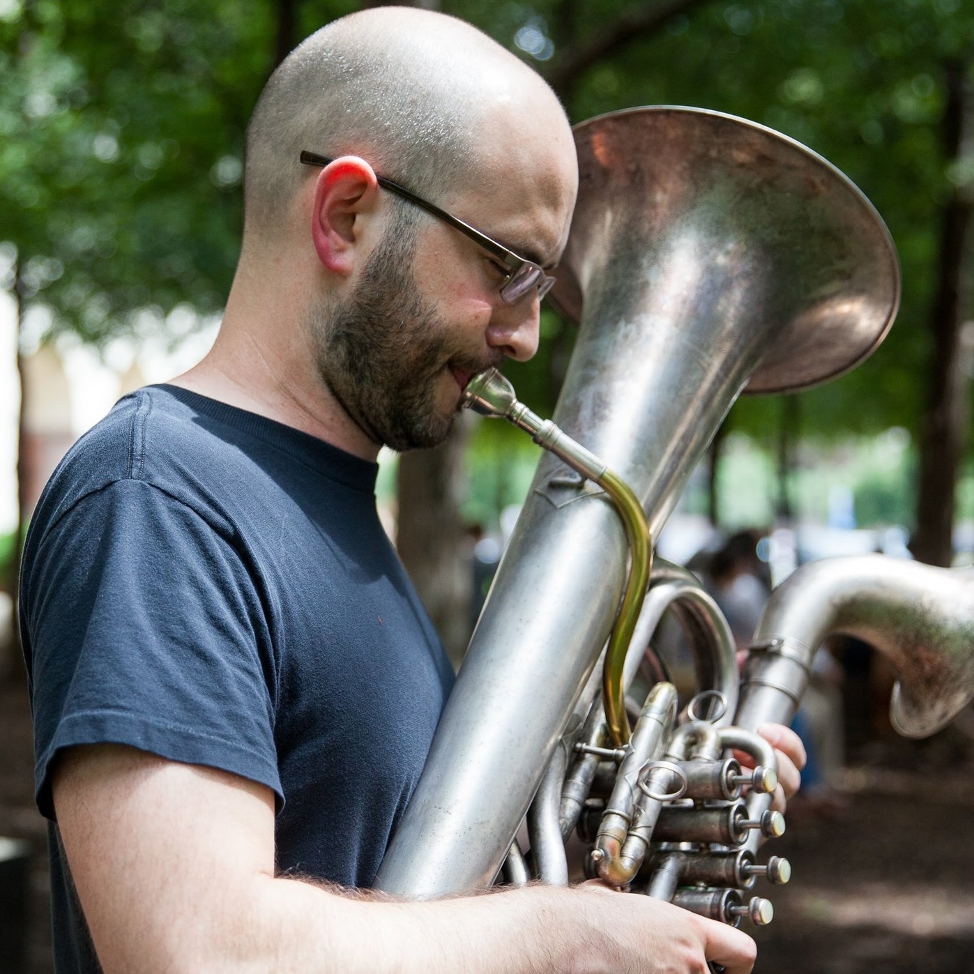 A bald man blowing into a brass instrument