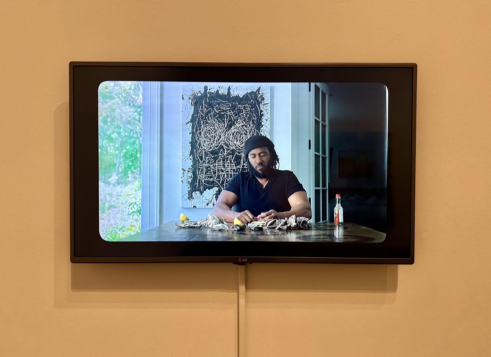 A video screen with a still of a Black man seated at a table, shucking oysters.