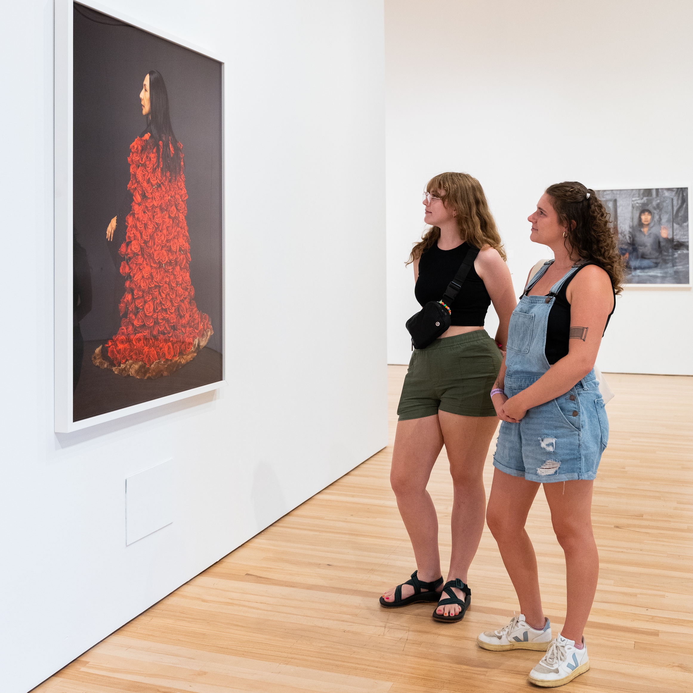 Two people looking at a large framed photo of a woman wearing a long cape constructed with red roses