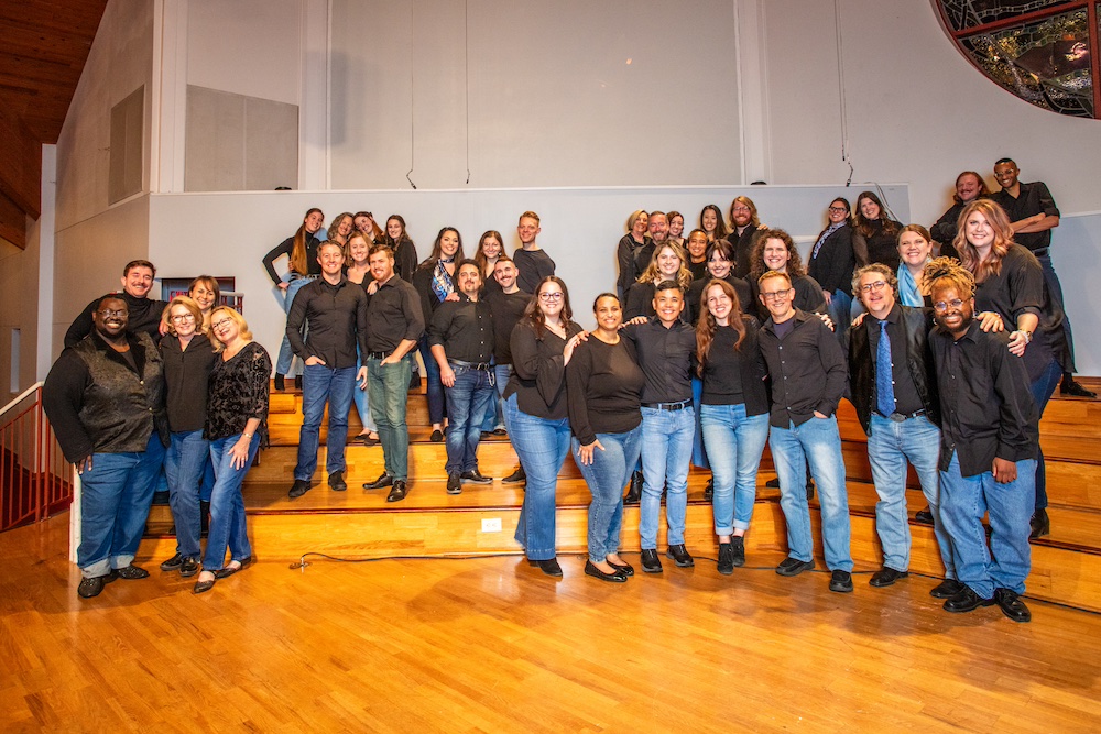 A large group of choir singers wearing jeans and dark tops