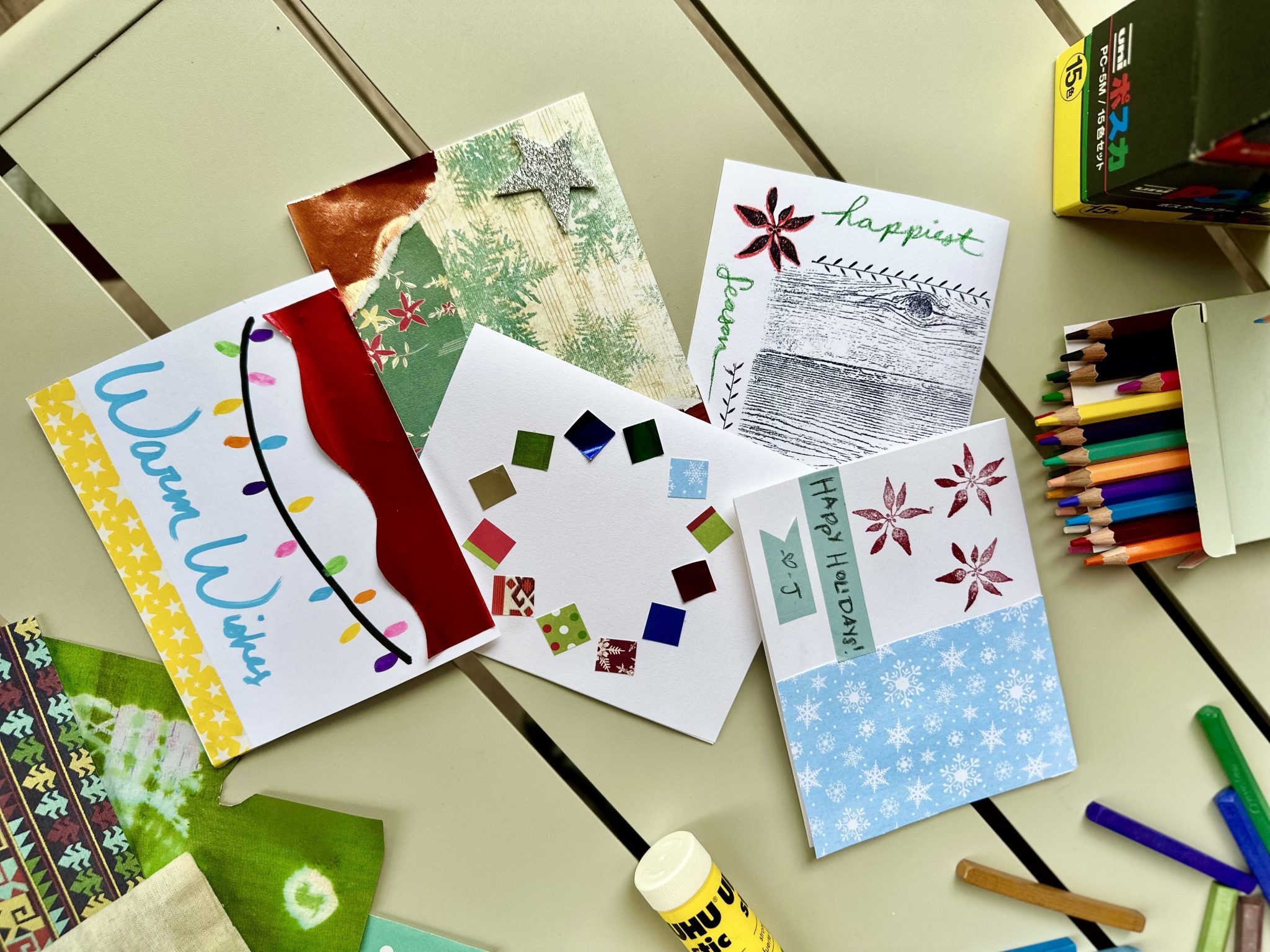 A selection of festive cards on a table with colouring pencils and glue nearby