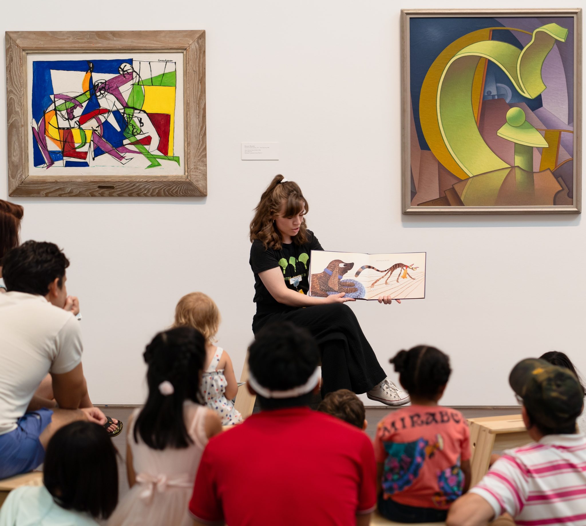 A person in a gallery reading a picture book to people