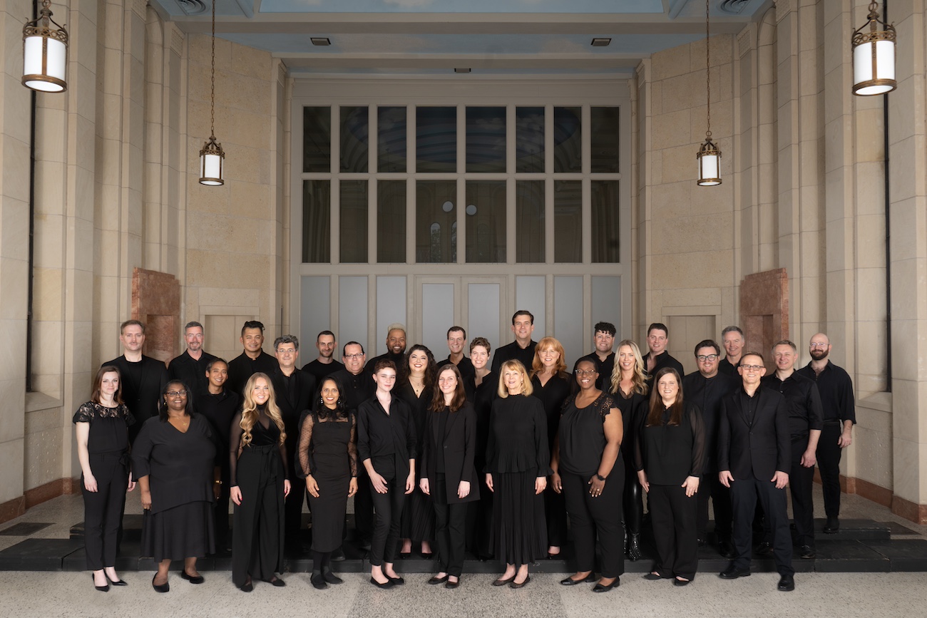 A group of choir singers, all wearing black and standing in front of a large doorway