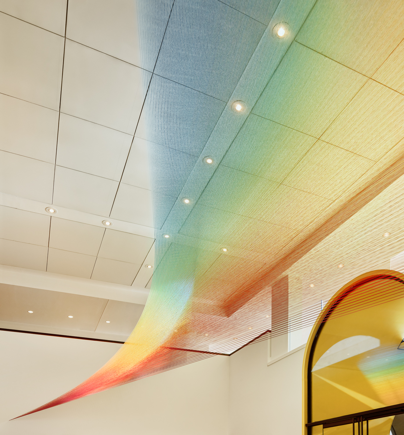 Interior view of the Blanton Museum of Art Check-in building featuring a colorful artistic installation made of thread that has kaliedoscopic colors, with subtle lighting enhancing its vibrancy.