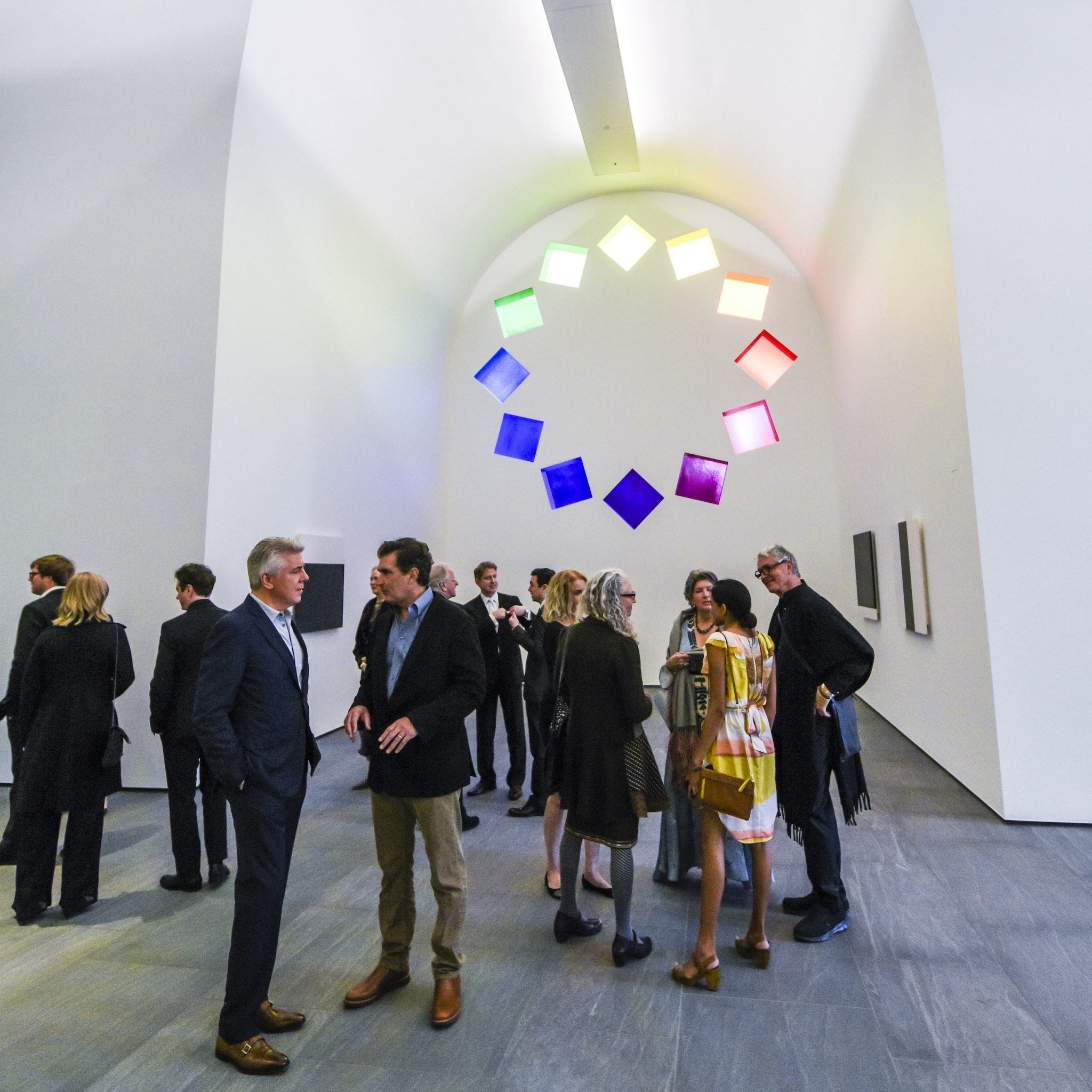 A group of people at an party inside "Austin" by Ellsworth Kelly which has colorful windows cascading in a circle