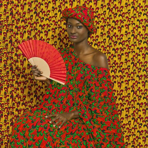 Photograph from the series The Studio of Vanities featuring a person holding a fan in brightly colored dress with patterns that repeat on the background