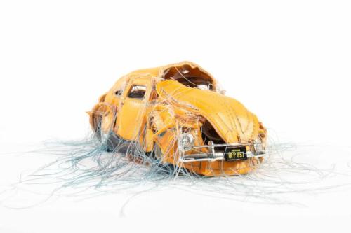A beat-up yellow car with silver threads coming out of its hood and doors