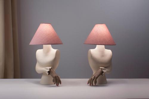 Two lamps side by sidewith pink lampshadesand bodies shaped likehuman torsos, each witha single hand emergingfrom a ruffled sleeve