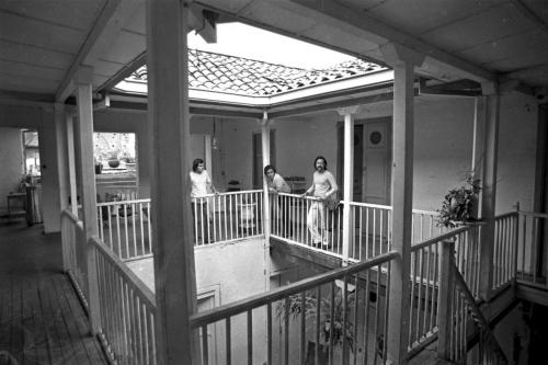 A black and white photo of a floor at the center of a building with banisters around the mezzanine and people standing next to them.