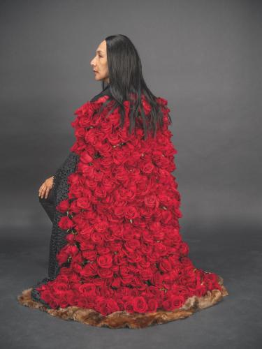An indigenous woman with long black hair wearing a floor length dress made of dozens of red roses