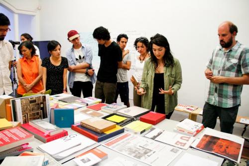 A group of people standing around a table. The table has a great number of books displayed.