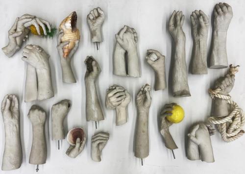 A variety of sculpted hands, come clutching different objects including shells