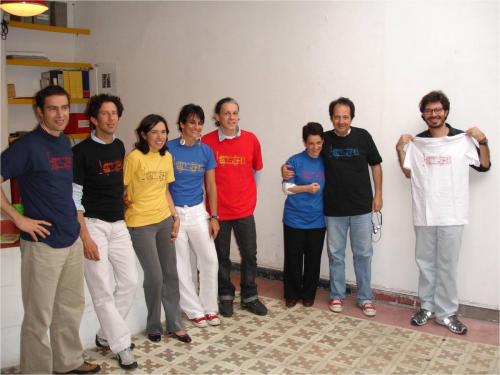 Color photograph of eight people standing. Two of them are hugging each other, posing for the picture.
