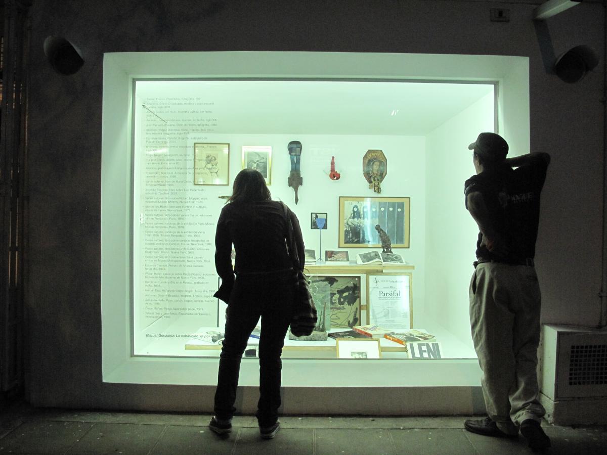 Dos personas mirando a través de un gran vidriera con diferentes objetos en su interior.